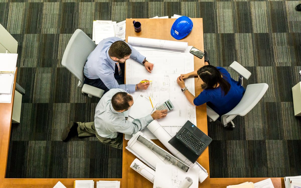 Three professionals reviewing building plans spread across a table